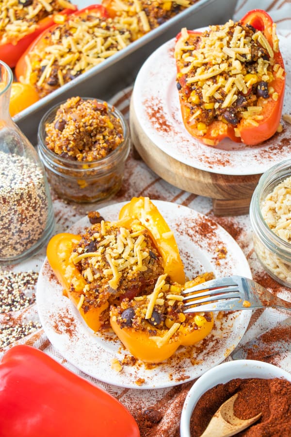 A yellow and red stuffed vegan pepper on two white plates with ingredients surrounding.