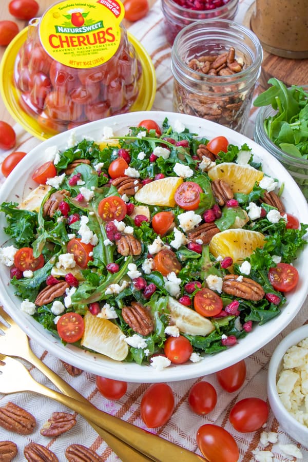 Colorful kale salad in white plate with yellow forks and tomatoes.