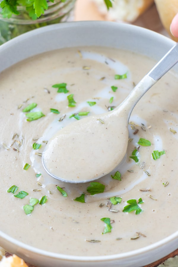 Silver spoon lifting creamy soup out of bowl.